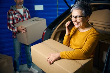 Gülümseyen bayan arabanın yanında otururken telefonda konuşuyor.