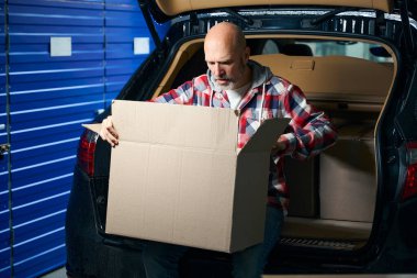 Ekose gömlekli adam kucağında büyük bir karton kutu tutuyor.