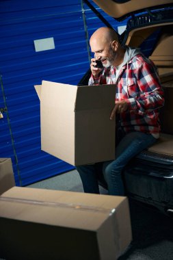 Elinde kutu olan kel bir adam telefonda konuşurken bir karton kutu tutuyor..