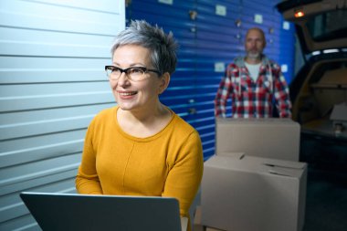 Bir kadın dizüstü bilgisayar tutuyor ve bir adam kutu taşıyor..