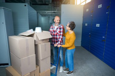 İki kişi büyük mavi bir nakliye arabasıyla bir şeyler taşıyor.