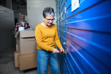 Kutuları olan kel adam deponun kapısını açan kadını bekliyor.