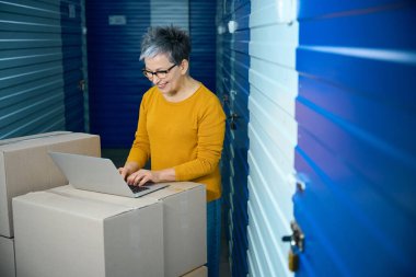Kadın, karton kutularda bir şeyler taşırken dizüstü bilgisayarda çalışıyor.