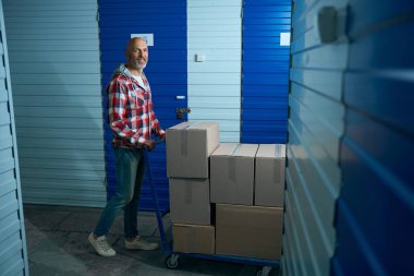 Kel kafalı ve ekose gömlekli bir adam mavi kargo arabasında karton kutular taşıyor.