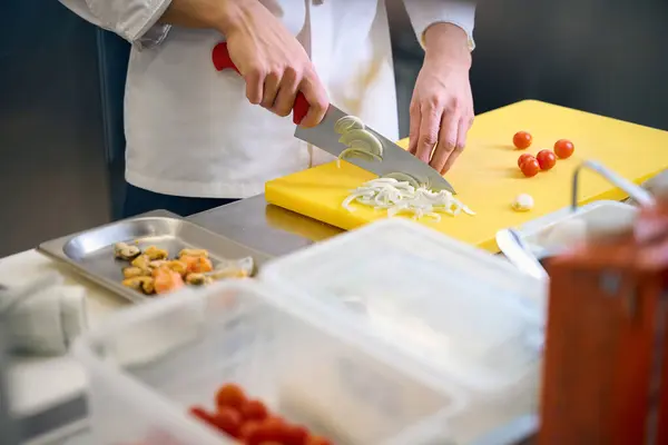 Kitchen staff cutting onions on a yellow cutting board, using a sharp knife