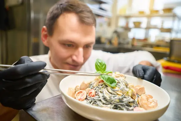 Chef Decora Espaguete Molho Com Folhas Manjericão Ele Trabalha Luvas — Fotografia de Stock