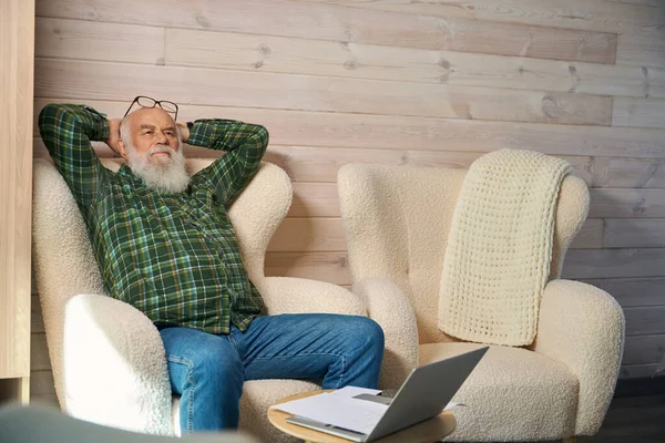 Old man is tired, working with documents in the living room, he is resting in a comfortable chair
