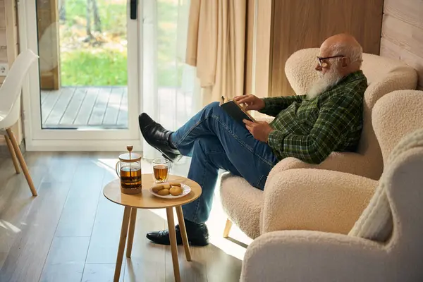 Starszy Mężczyzna Okularach Siedzi Książką Wygodnym Fotelu Francuskie Okno Wychodzi — Zdjęcie stockowe