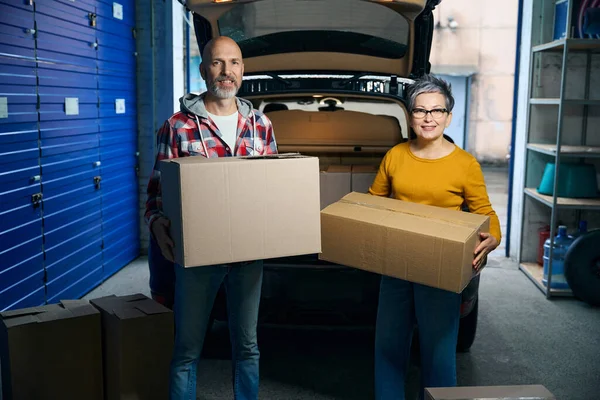 Yetişkin insanlar ellerinde karton kutularla kameraya bakıyorlar.