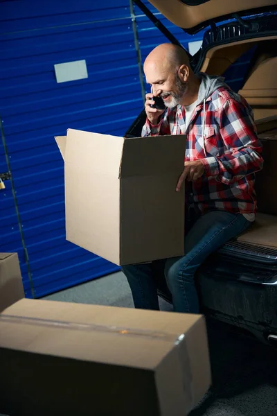 Elinde kutu olan kel bir adam telefonda konuşurken bir karton kutu tutuyor..