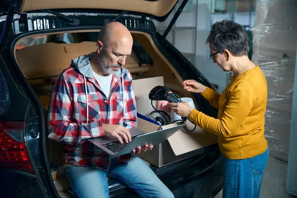 Kısa saçlı bir kadın, bir arabanın bagajındaki kutulara bakıyor..