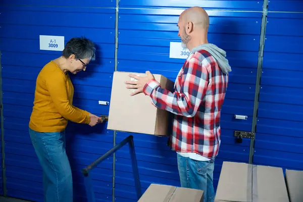 Bald guy holding a box with things while a woman opens the door to the storage room