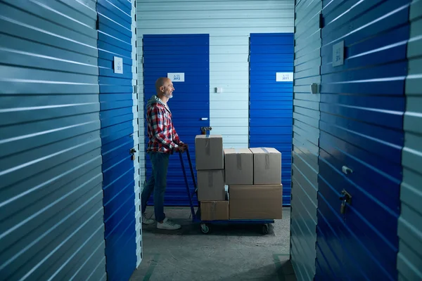 Kareli gömlekli bir adam eşyaları depoya taşır.