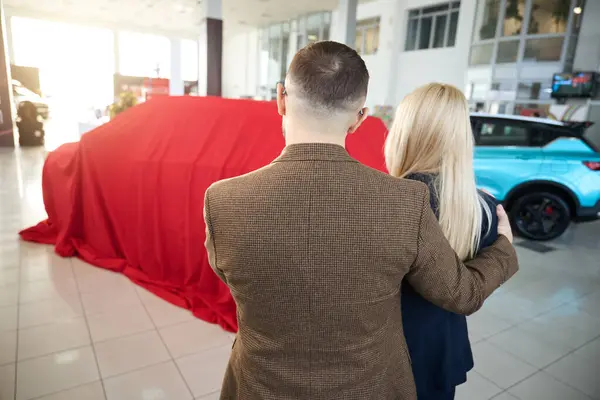 夫と妻は赤いギフトケースに包まれた新しい車を見ます — ストック写真