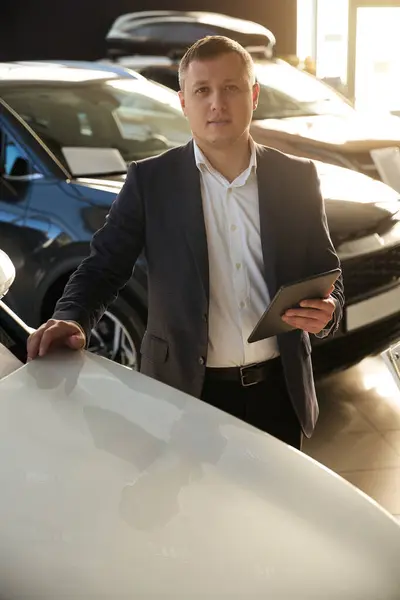 Car salesman stands next to a new car at a car sales center