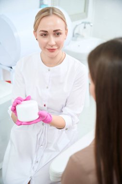 Kozmetik uzmanı elinde kremayla şişeyi müşteriye sunuyor. Deri ve vücut bakımı