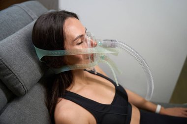 Spor elbiseli bir kadının portresi rahat koltuğa uzanmış, hipoksik terapi görüyor.