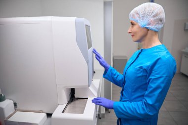 Kadın bulaşıcı hastalıklar uzmanı modern ekipman laboratuvarında çalışıyor. Mavi üniformalı bir kadın.