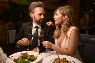 Sıcak bir restoranda romantik bir akşam yemeği yiyen çift, hafif salata ve şarap servis edilir.
