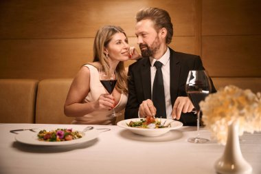 Lokantada romantik bir akşam yemeği yerken orta yaşlı bir çift iletişim kuruyor. Kadının yakası kalın.