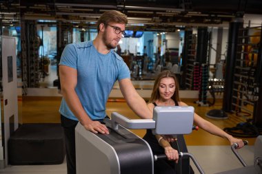 Antrenör gözetiminde bir simülatör üzerinde kadın egzersizleri, spor salonu modern ekipmanlara sahiptir.