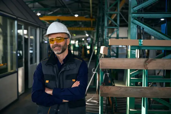 Man in safety glasses and a hard hat stands in a production workshop, safety precautions are observed in window production