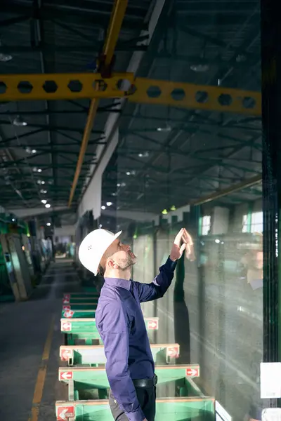 Engineer inspects glass in a production workshop, high-tech equipment is used in window production