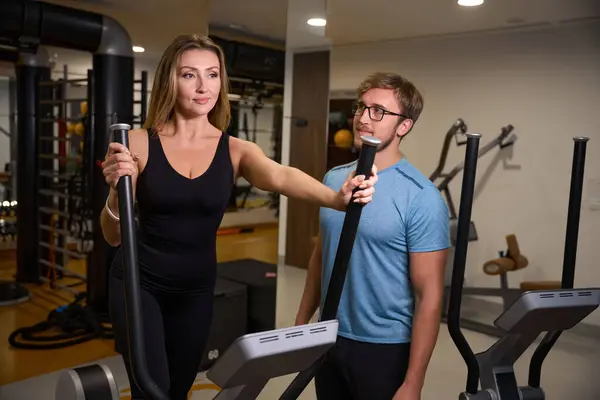Woman works out on a walking machine under the supervision of an instructor, in the gym there is modern equipment