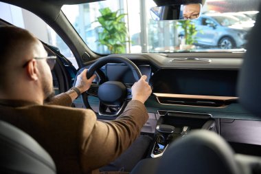 Adam yeni bir arabanın direksiyonunu elinde tutuyor.