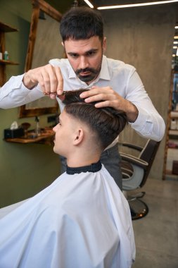 Profesyonel berber, berber dükkanındaki adam için şık saç stili yapıyor.