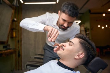 Kuaför kuaförde müşterilerin bıyıklarını kesiyor.