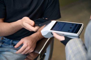 Berber dükkanında saç kesimi için akıllı telefon ve postiş terminaliyle ödeme yapan tanınmamış bir müşteri.