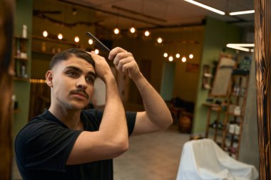 Çekici berber müşterileri beklerken berber dükkanında kendini tarıyor.