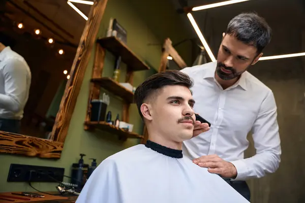 Barber using hair clipper for making stylish hairstyle at barbershop
