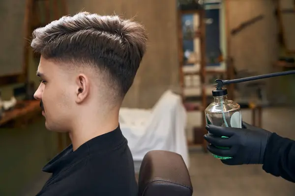 ヴィンテージデザインのスタイリッシュなボトルから男のバーバーが香水バーショップでクライアントの髪の上に — ストック写真