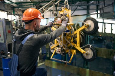 Adam bir pencere yapım atölyesinde çalışıyor, elektrikli süpürge kullanıyor.