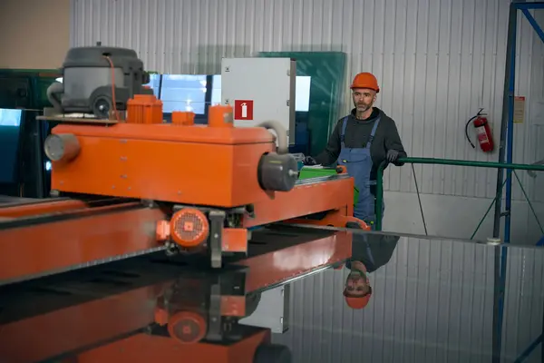 Man uses an automatic glass cutting table in a window production, a worker wearing a hard hat and protective gloves.