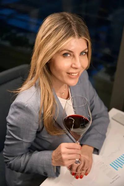Smiling lady enjoying red wine, she is wearing an elegant business suit