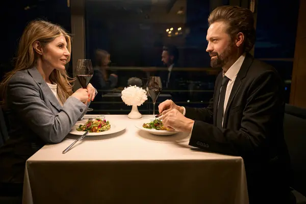 Female and a male are talking over dinner in a cozy restaurant, they are in elegant business suits