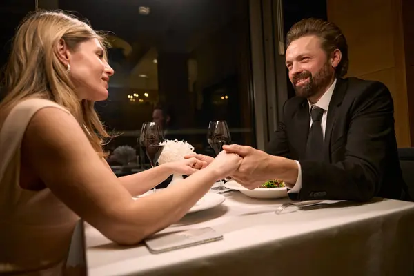 Couple sits at a table in a restaurant, people hold hands
