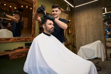 Profesyonel berber, berber dükkanındaki müşterisinin saç stili için makas kullanıyor.