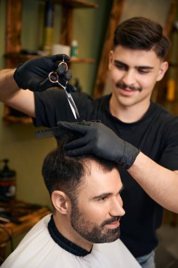 Yetenekli kuaför, profesyonel berber dükkanında makaslarla yeni bir görünüm yaratıyor.