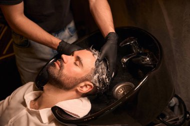 Berber dükkanındaki yakışıklı müşterisine saç yıkayan kuaför.