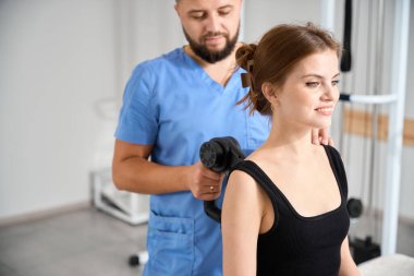 Doktor hastalara masaj yapıyor. Özel bir masaj aleti, rahat kıyafetler giyen bir kadın.