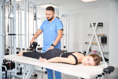 Doktor, rehabilitasyon merkezinin spor salonunda hasta bacaklarına masaj yapıyor.