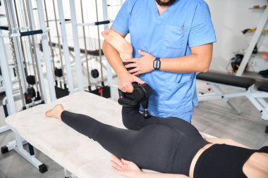 Uzman, bir rehabilitasyon merkezinde özel bir masaj aleti ile hasta vücuduna masaj yapıyor.