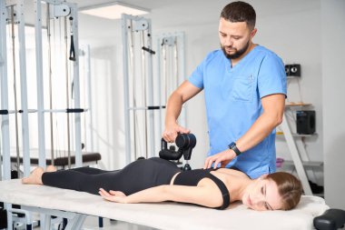 Kinesiyoterapi kliniğinin çalışanı bir hastanın vücuduna masaj yapar, özel bir masaj aleti kullanır.