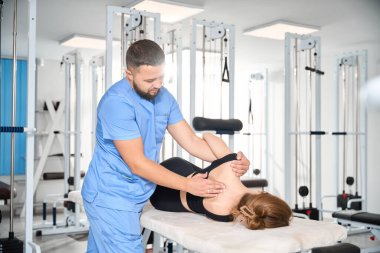 Kayropraktik uzmanı rehabilitasyon merkezinde bir hastayla çalışıyor. Rahat bir eğitim kıyafeti giymiş bir kadın.