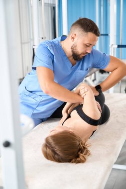 Bir kineziyoloji kliniğinin çalışanı genç bir kadının omurgasıyla çalışır, hasta masaj masasında yatar.