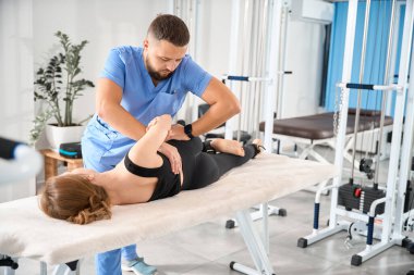 Bir kineziyoloji kliniğinin çalışanı genç bir hastanın omurgasıyla çalışır, kadın masaj masasında yatar.